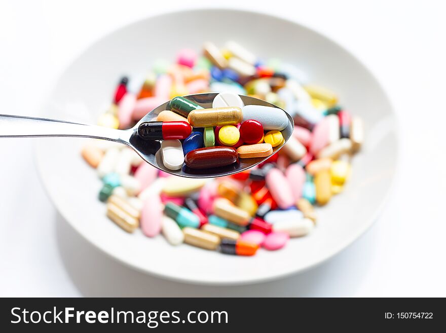 Various types of tablets, capsules and pills on  spoon with colorful medicine background