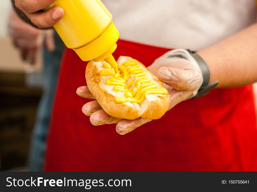 Hands of street chef puts mustard on a hot dog bun close up. Hands of street chef puts mustard on a hot dog bun close up
