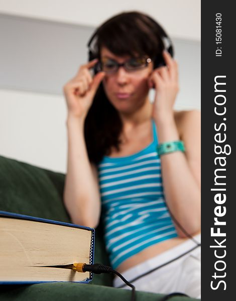 Pretty girl sitting on a sofa and listening to a book. Focus on book. Pretty girl sitting on a sofa and listening to a book. Focus on book