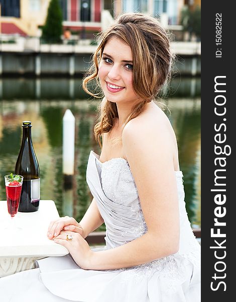 An attractive young woman is smiling and wearing formal attire while sitting at a dockside table with an alcoholic beverage. Vertical shot. An attractive young woman is smiling and wearing formal attire while sitting at a dockside table with an alcoholic beverage. Vertical shot.