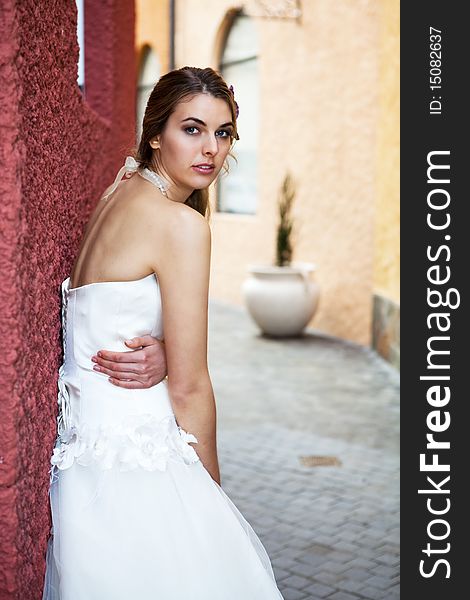 An attractive young woman wearing a white wedding dress is standing in a brick alley leaning on a red wall. Vertical shot. An attractive young woman wearing a white wedding dress is standing in a brick alley leaning on a red wall. Vertical shot.