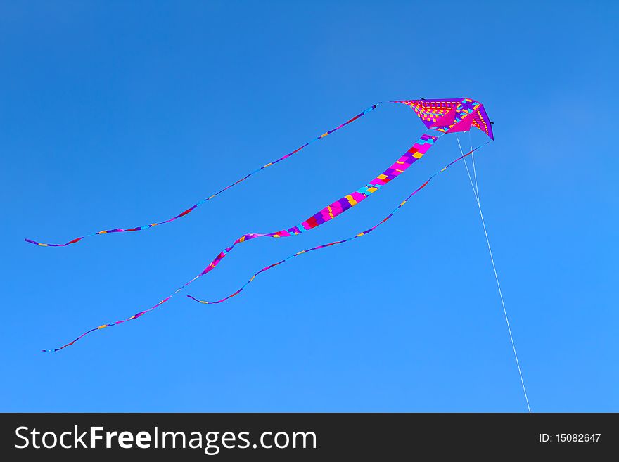 Colorful kite flying high in bright blue sky.