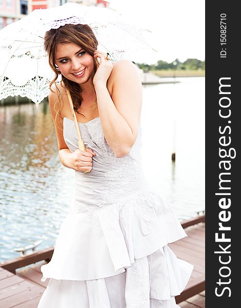 An attractive young woman in a gown is smiling and holding a parasol near the water. Vertical shot. An attractive young woman in a gown is smiling and holding a parasol near the water. Vertical shot.