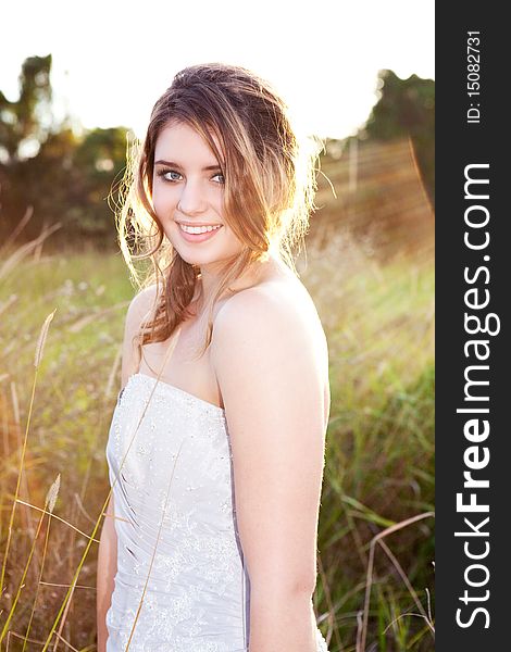 An attractive young woman wearing formal attire is standing in a grass field. Vertical shot. An attractive young woman wearing formal attire is standing in a grass field. Vertical shot.