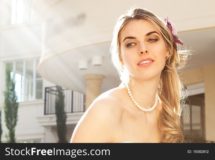 An attractive young woman wearing pearls smiles with sunlight beaming down on her. Horizontal shot. An attractive young woman wearing pearls smiles with sunlight beaming down on her. Horizontal shot.
