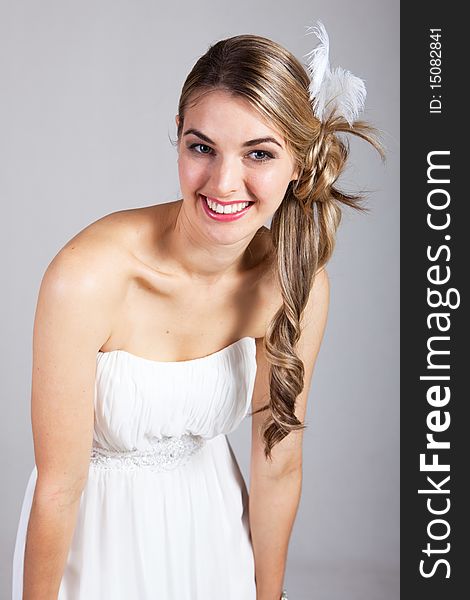 Attractive young woman wearing a white strapless dress and a feather hairpiece poses and smiles. Vertical shot. Attractive young woman wearing a white strapless dress and a feather hairpiece poses and smiles. Vertical shot.