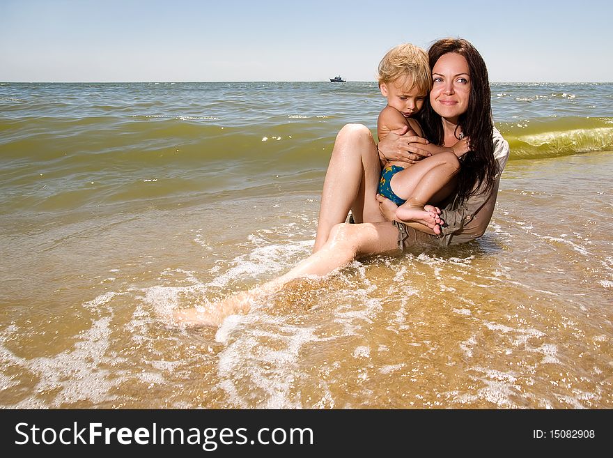 Young mom holds her little son in hands sitting in water of a sea. Young mom holds her little son in hands sitting in water of a sea