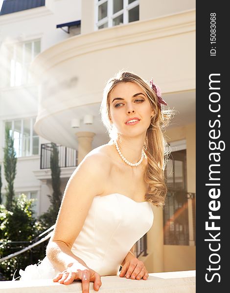 An attractive young woman is wearing a white dress and pearls and is smiling. She is looking over a railing. Vertical shot. An attractive young woman is wearing a white dress and pearls and is smiling. She is looking over a railing. Vertical shot.