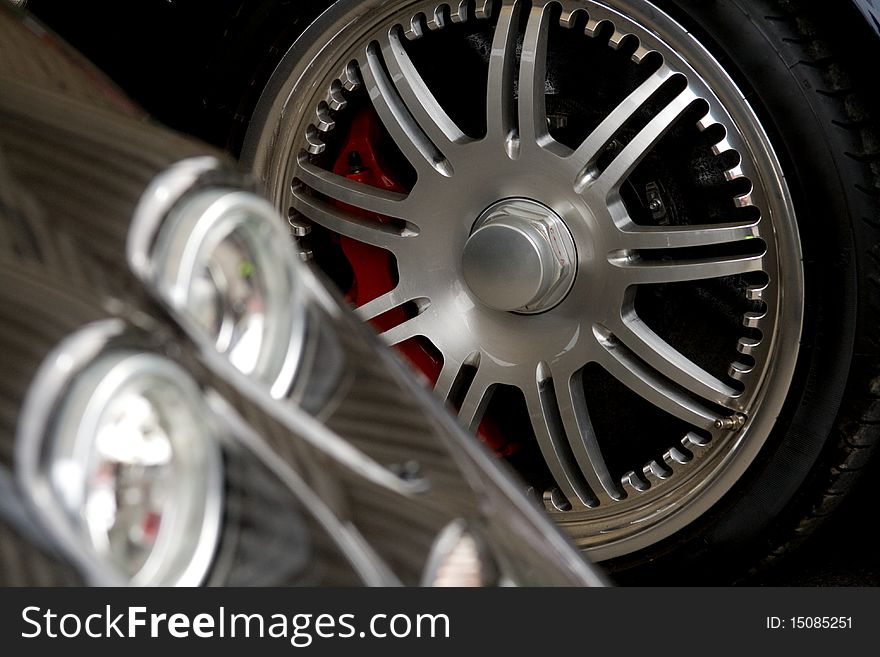 Exotic car headlight with chrome wheel in the background