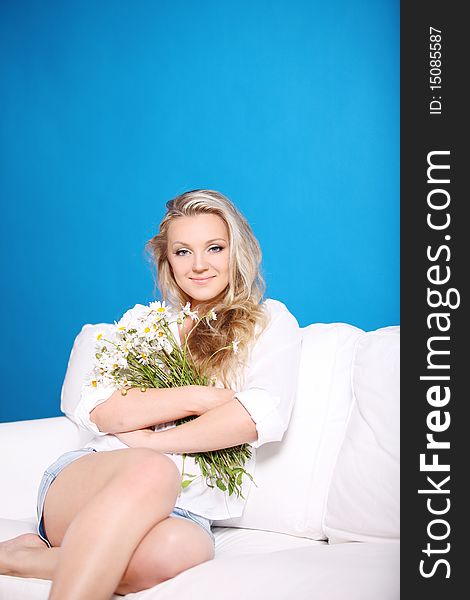 Girl with a bouquet of camomiles sits on a sofa