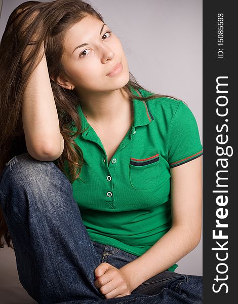 The beautiful young woman sits having reflected on a grey background. The beautiful young woman sits having reflected on a grey background.