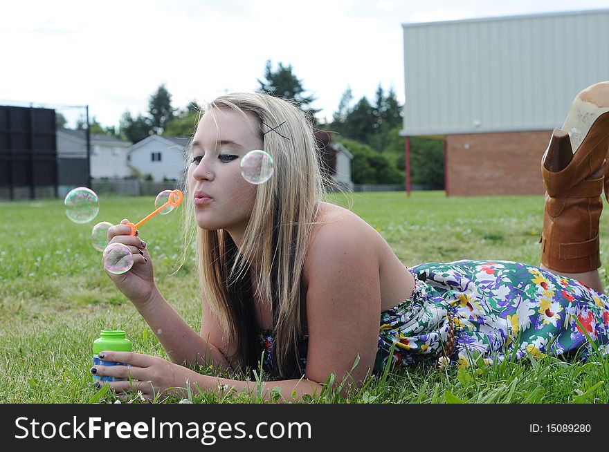 Young white Caucasian teenage girl laying in grass blowing bubbles playfully. Young white Caucasian teenage girl laying in grass blowing bubbles playfully.
