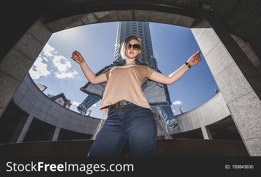 The concept of modern urban fashion. The girl throws off her denim jacket, arms raised high.