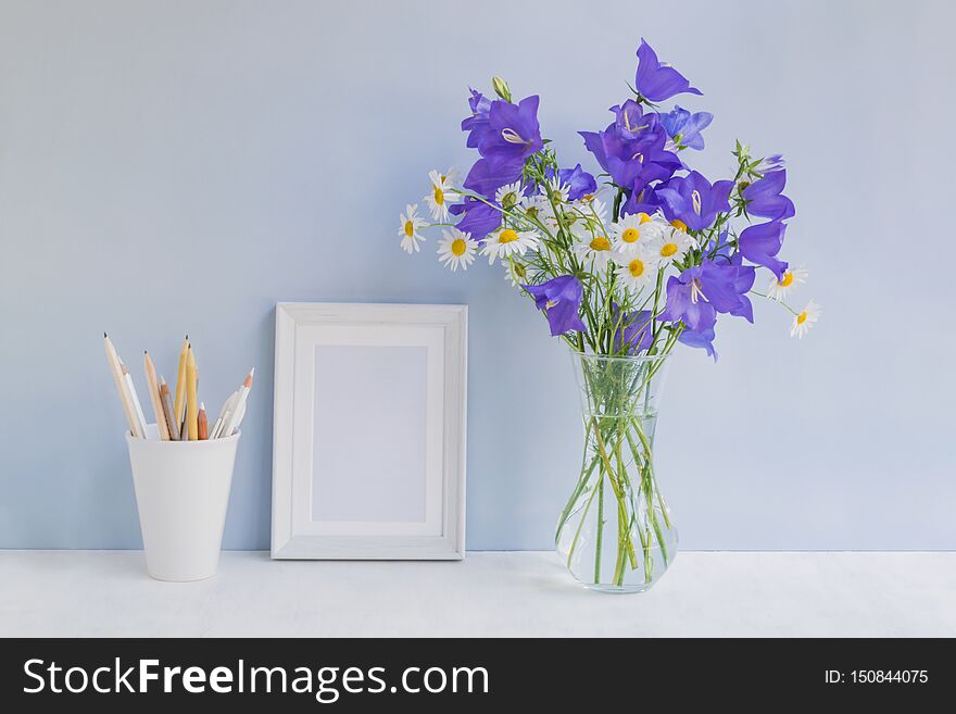 Mockup with a white frame and summer blue flowers in a vase on a light blue background