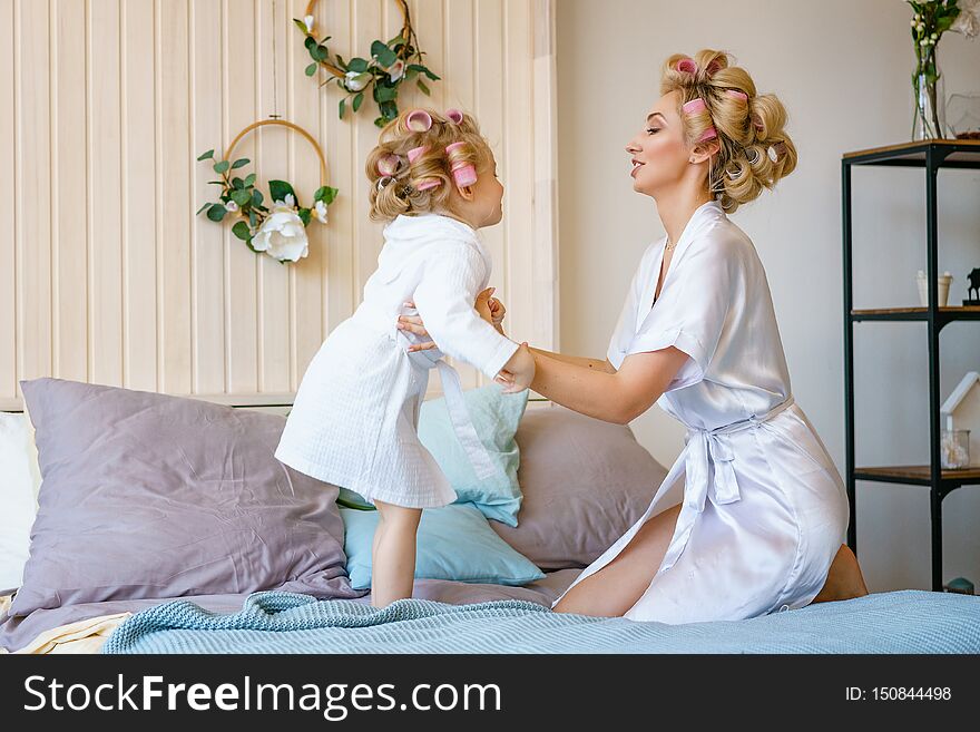 Happy mom and daughter having fun on the bed in dressing gowns