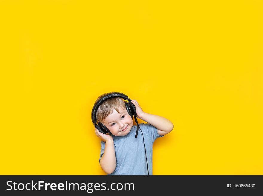 Little cute caucasian blonde boy in headphones posing happy smiling  on yellow background