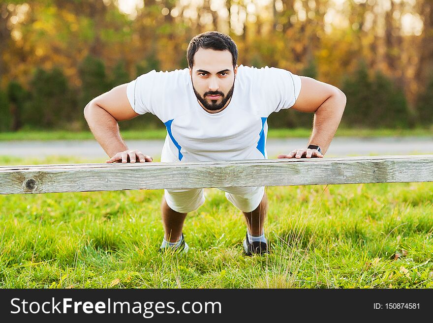 Portrait sporty man 30s in sportswear doing push-ups in green park.