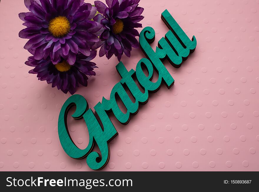 Purple flowers and a wooden painted word laid on a pink textured background. Purple flowers and a wooden painted word laid on a pink textured background.