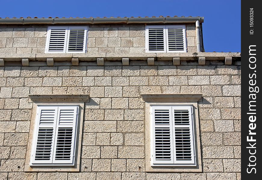 Details of the stony building facade with white shutters.