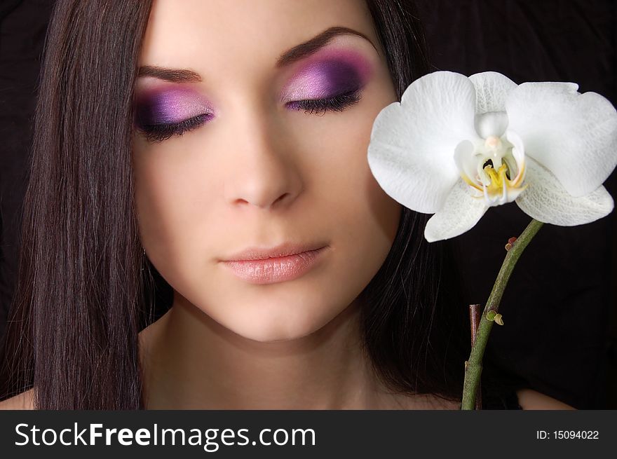 Beautiful brunette with orchid flower eyes closed isolated on black