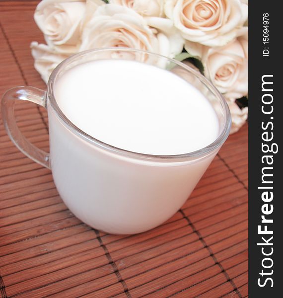 Cup of fresh,white milk and creamy roses isolated on wooden background. Cup of fresh,white milk and creamy roses isolated on wooden background