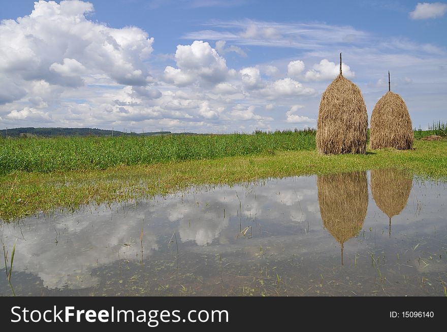 Hay in stacks and clouds are displayed in water of a pool after long rains. Hay in stacks and clouds are displayed in water of a pool after long rains