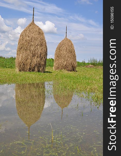 Hay in stacks and clouds are displayed in water of a pool after long rains. Hay in stacks and clouds are displayed in water of a pool after long rains