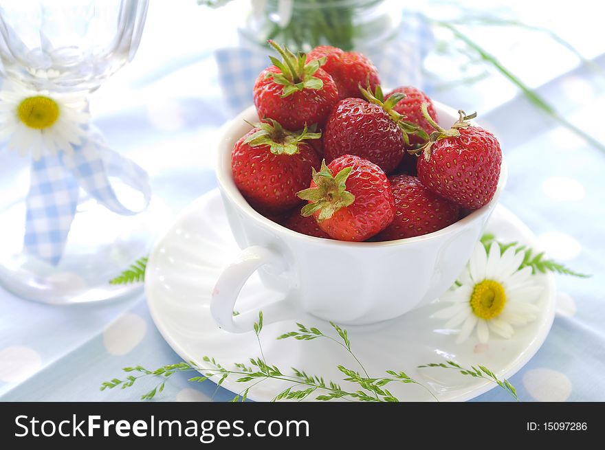 A cup of strawberries with daisy on light blue background. A cup of strawberries with daisy on light blue background