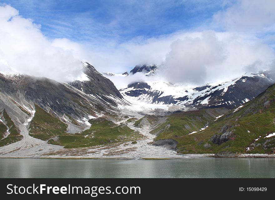 Scenic view of snowy mountains and sunshine in Alaska. Blue sky peeking through clouds. Scenic view of snowy mountains and sunshine in Alaska. Blue sky peeking through clouds.