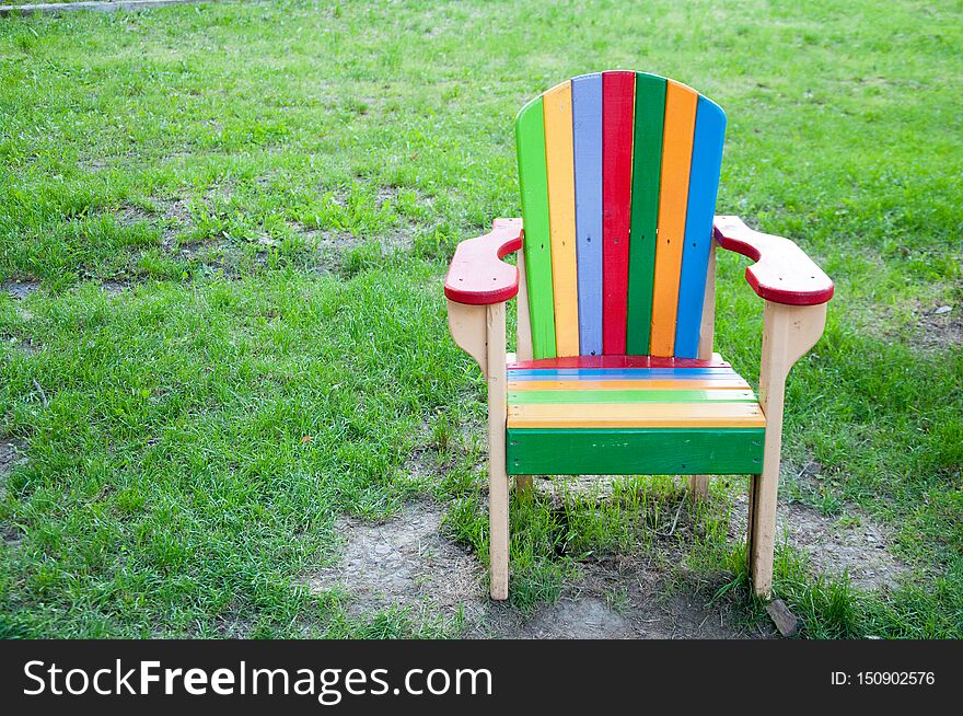 A multi-colored wooden chair on the playground. On the background of green grass