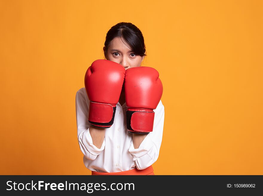 Young Asian woman with red boxing gloves on yellow background