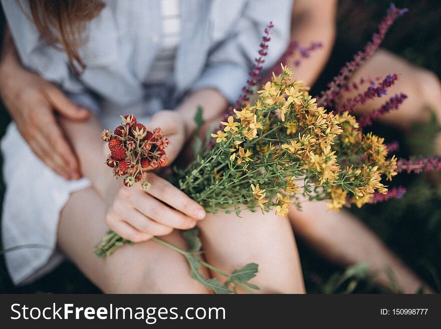 Girl`s and boy`s hands and legs holding together holding flowers and wild berries in summer. Girl`s and boy`s hands and legs holding together holding flowers and wild berries in summer