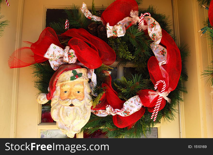 Santa Door Wreath adorning a door for Christmas.  It's 

trimmed with wide red ribbon, candy canes, an d a large 

Santa face.