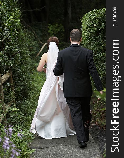 Bride and groom on their wedding day walking away from the camera down a path overgrown with trees. Bride and groom on their wedding day walking away from the camera down a path overgrown with trees