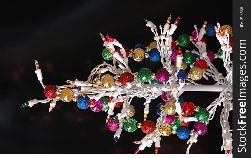 A white wire christmas tree with lights and multi colored garland against a black background