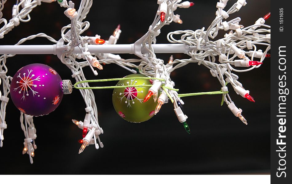 A white wire christmas tree with lights and purple and green ball ornamnets against a black background. A white wire christmas tree with lights and purple and green ball ornamnets against a black background