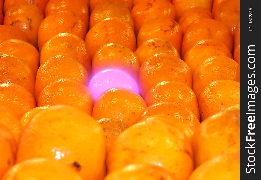 Purple glowing mandarin orange in rows of 'normal' mandarin oranges. Purple glowing mandarin orange in rows of 'normal' mandarin oranges.