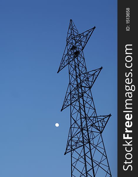 Moon in blue sky above electricity pylon, low angle view