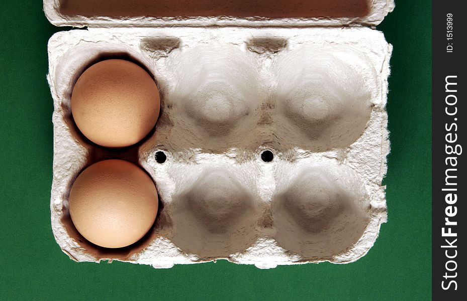 Two Brown Eggs In A Grey Cardboard Box On Green Background. Two Brown Eggs In A Grey Cardboard Box On Green Background