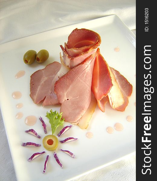 Smoked ham slices arranged on a plate with olive and lettuce decoration