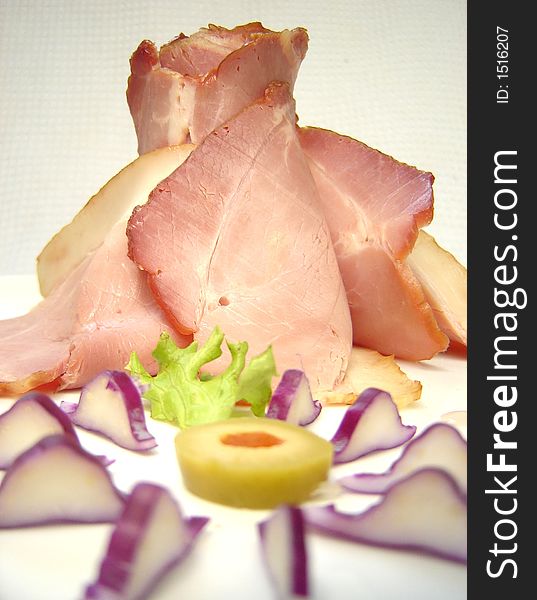 Smoked ham slices arranged on a plate with olive and lettuce decoration