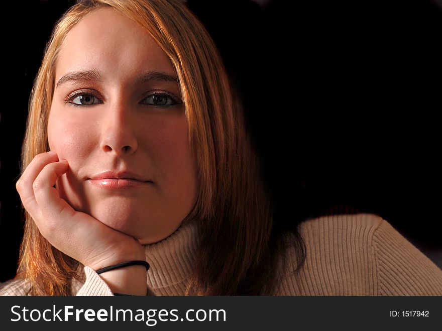 Attractive young woman with her chin resting on her hand against a black background