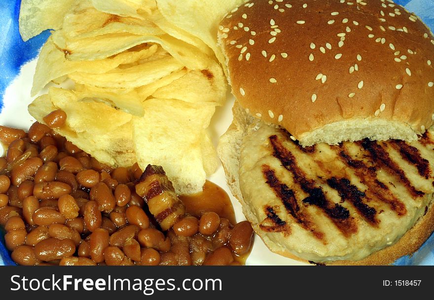 This is a close up image of a Turkey Burger with Potato Chips and Baked Beans. This is a close up image of a Turkey Burger with Potato Chips and Baked Beans.