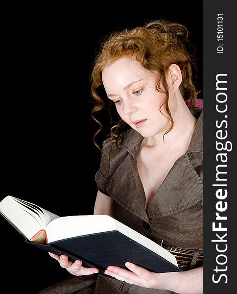 Beautiful girl with red hair reading a book, seen against black background