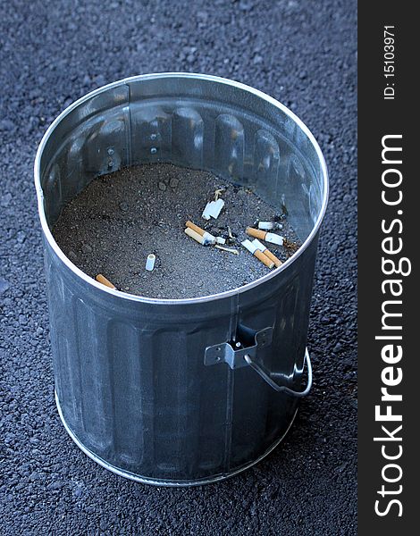 A small bucket used as a cigarette ashtray, filled with sand and used cigarette butts visible inside. A small bucket used as a cigarette ashtray, filled with sand and used cigarette butts visible inside.