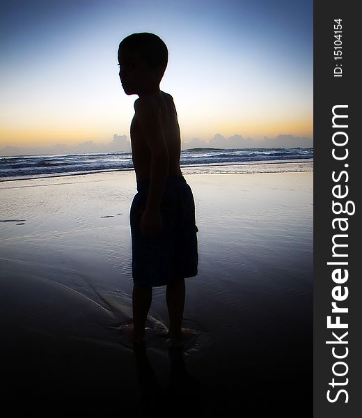 A young boy stands in the ocean as he waits for the sun to rise in florida. A young boy stands in the ocean as he waits for the sun to rise in florida