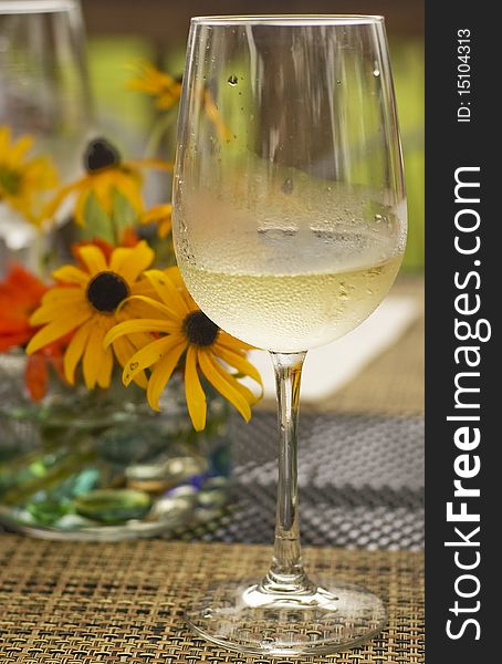 Glass of chilled white wine standing on a rustic mat with yellow flowers on the background