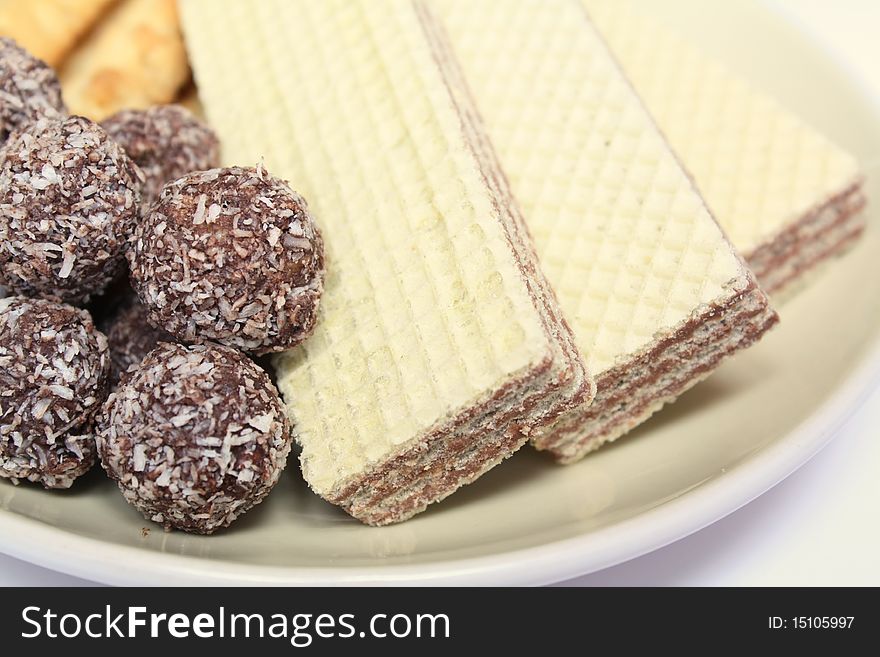 Various confectionery on plate, chocolate balls, wafer witch chocolate layers and cookies on white background