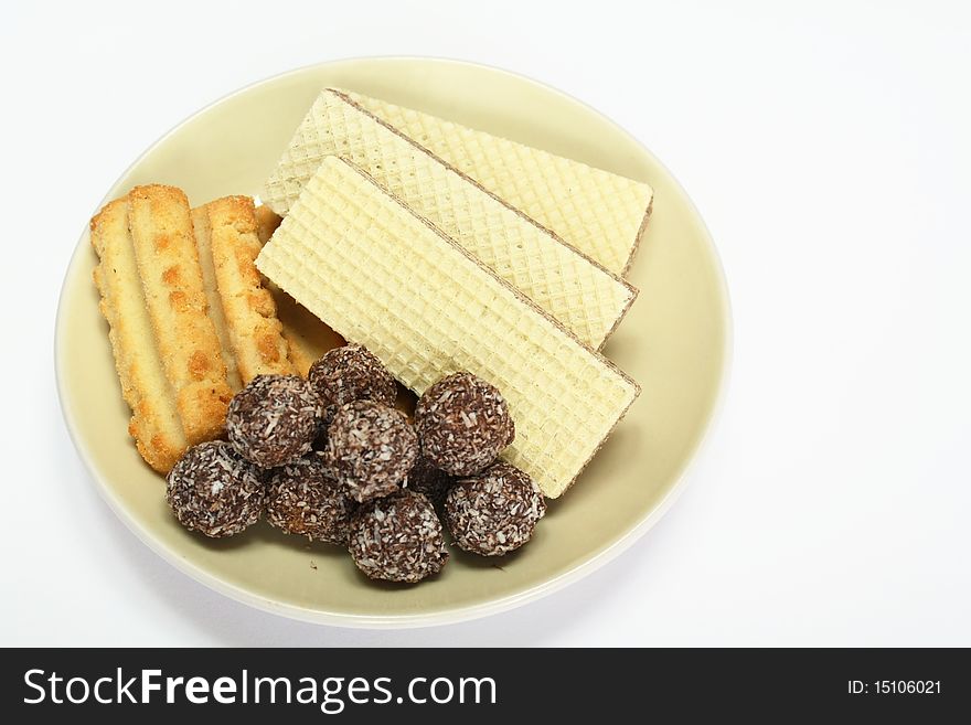 Various confectionery on plate, chocolate balls, wafer witch chocolate layers and cookies on white background