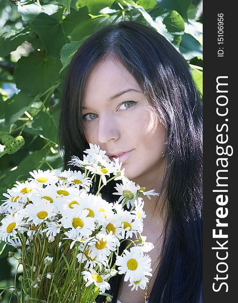 A girl gets on the hip the bouquet of camomiles. Photo on a background trees.